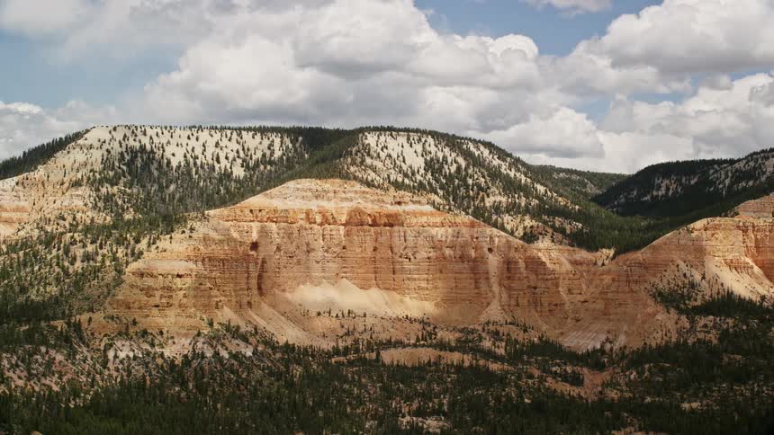 Aerial footage showcases the magnificent Barney Top Mesa in Utah with desert vegetation and stunning views of the surrounding mountains captured during a partly cloudy day in the Southwest United States