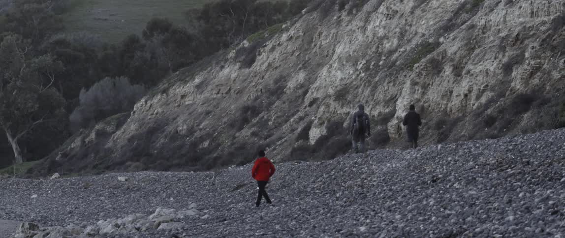 People hike along the rocks near a large hill