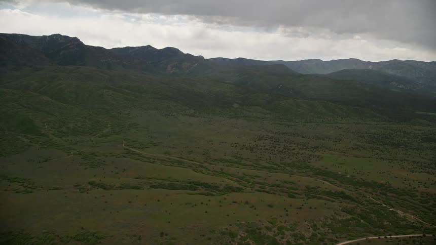 Approaching green hills and heavy clouds above the Wasatch Range in Utah captured inaerial footage during a cloudy day in the Southwest United States