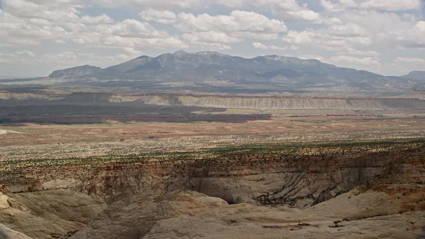  aerial footage of flying by distant mesas and mountains in Capitol Reef National Park showcasing the arid and famous desert landscape of Utah during a partly cloudy summer day