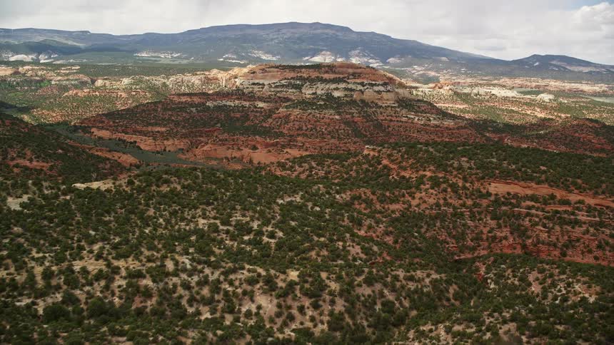 Aerial footage of desert hills covered in vegetation approaching a peak in Capitol Reef National Park Utah on a partly cloudy day in summer
