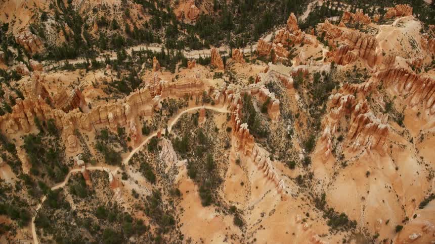 Aerial footage of dirt roads winding through badlands with hoodoos buttes and a dry riverbed in Bryce Canyon National Park Utah