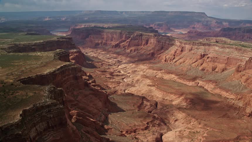 Aerial footage of a wide canyon between mesas on the Navajo Nation Reservation in Utah with partly cloudy skies and a dry riverbed visible shot over Southwest United States during summer