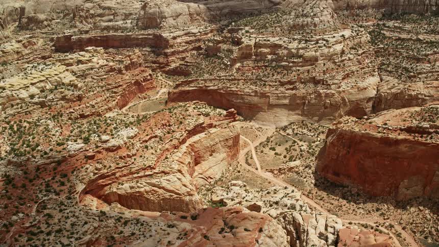 In thisaerial footage experience a bird's eye view of a dirt road winding through a majestic canyon in Capitol Reef National Park Utah with parked cars and breathtaking landscapes