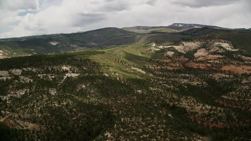 Flying over low green mountains in Dixie National Forest Utah thisaerial footage captures the breathtaking natural beauty of the Southwest United States during a partly cloudy summer day