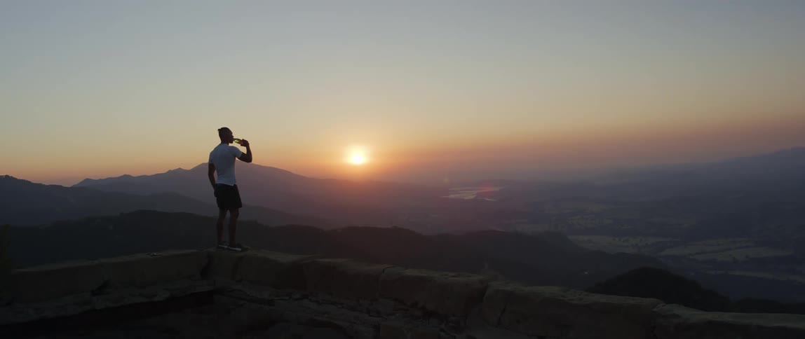 A man drinking water watching the landscape at sunset