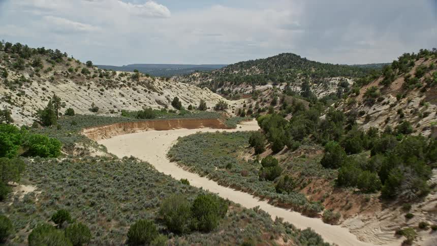  aerial footage capturing a dry riverbed in the hills of Grand Staircase-Escalante National Monument Utah with partly cloudy skies and low flying over the wild landscape during summer