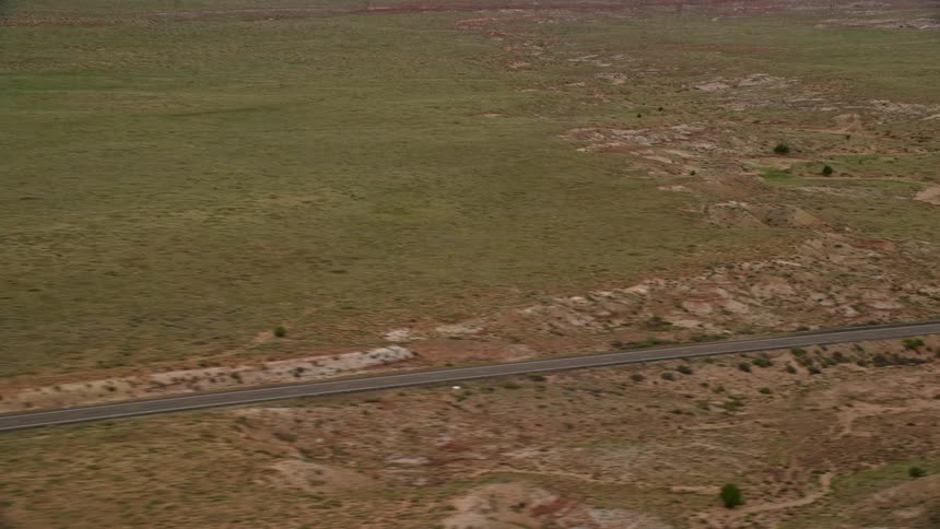 Aerial footage of a deserted highway cutting through a sunlit desert plain in Glen Canyon National Recreation Area Utah and Arizona