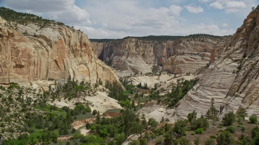 aerial footage capturing the mesmerizing flight through a narrow canyon surrounded by lush green vegetation in the Grand Staircase-Escalante National Monument Utah during a partly cloudy day in the summer