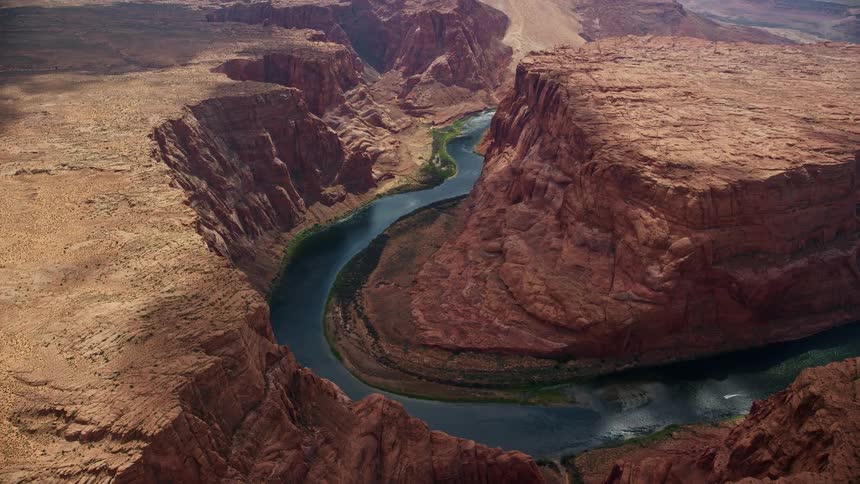 Aerial footage of a boat approaching a bend in the canyon tilting down to reveal the Colorado River in Glen Canyon Arizona during the daytime in Utah summer