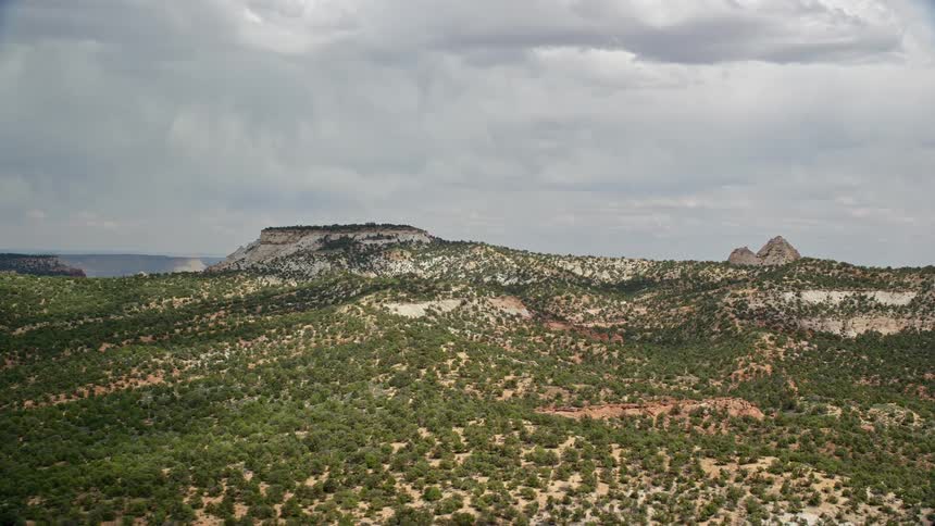 aerial footage of flying over a small mesa in the Grand Staircase-Escalante National Monument Utah showcasing the arid desert landscape and stunning views of the surrounding mountains and hills during a partly cloudy day in the Southwest United States