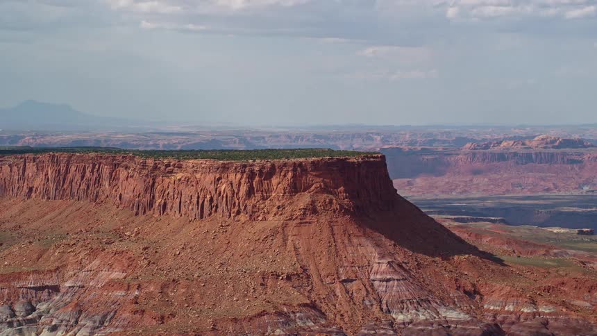 Aerial footage of a tall desert mesa on the Navajo Nation Reservation in Arizona and Utah showcasing the breathtaking landscape of the Southwest United States with green grass on top under a bright sunny day