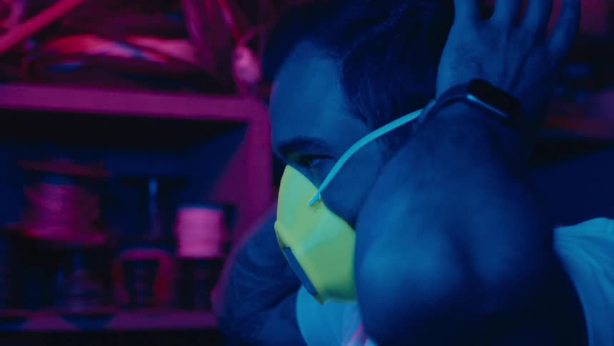 A man puts on a mask as lights flash and then the mask lights up