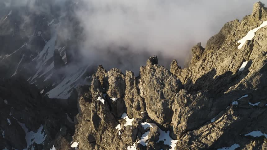 Low lying clouds obscure park of mountain range while snow speckles slopes