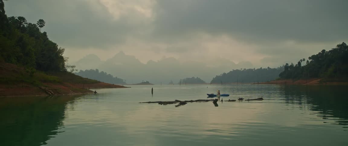 A person kayaks across a lake on cloudy day