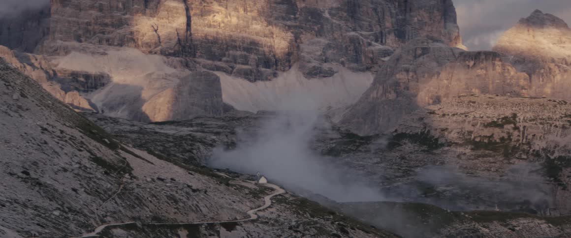 Fog flows between mountains and onto winding road near building