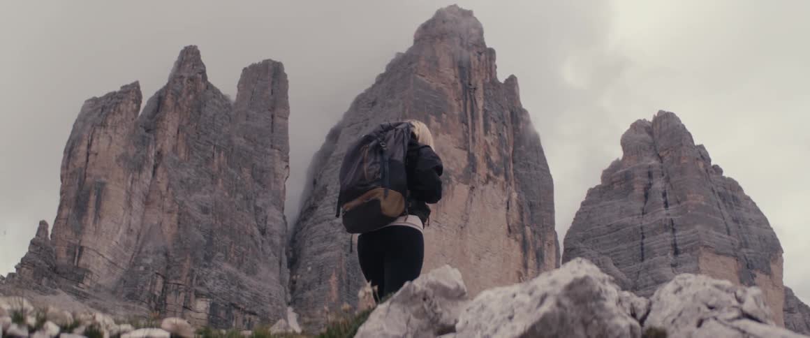 A woman wearing a backpack hikes up a rocky mountain path