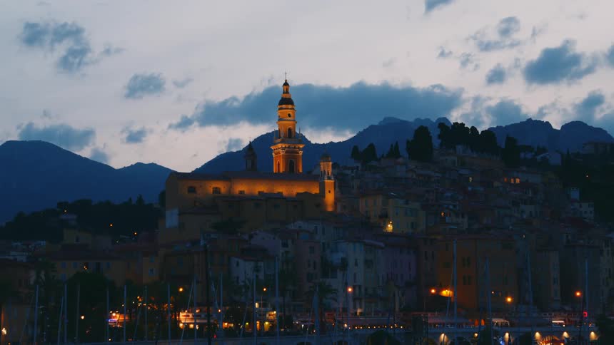 Lights glow at the basilica of saint michel archange of menton with mountains in the distance