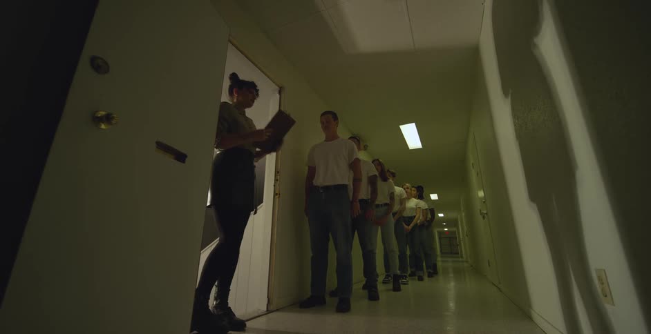 A woman summons the first person in line from a group standing in a corridor