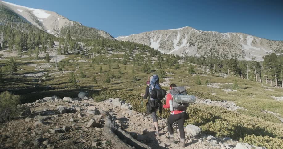 Two hikers wearing backpacks and using poles walk a rocky trail