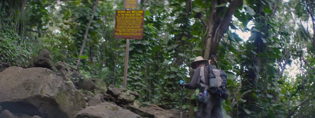 Man using walking sticks hikes up a rocky path
