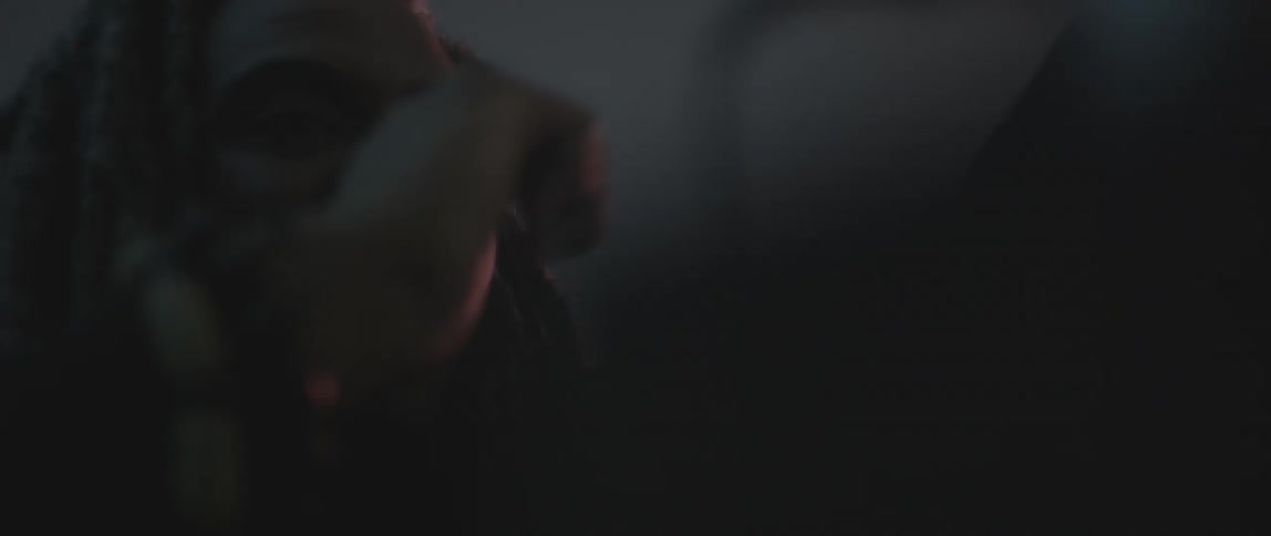 A man with dreadlocks scratches his nose and then reaches forward