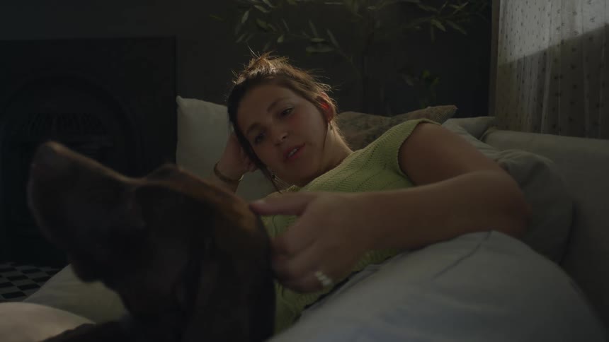 Woman lying on the sofa alongside her dog affectionately petting its head