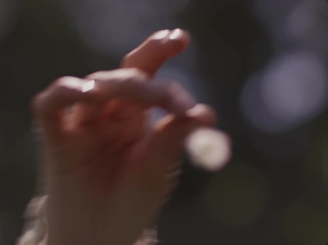 A child is reaching for a small flower a woman is holding in her fingers