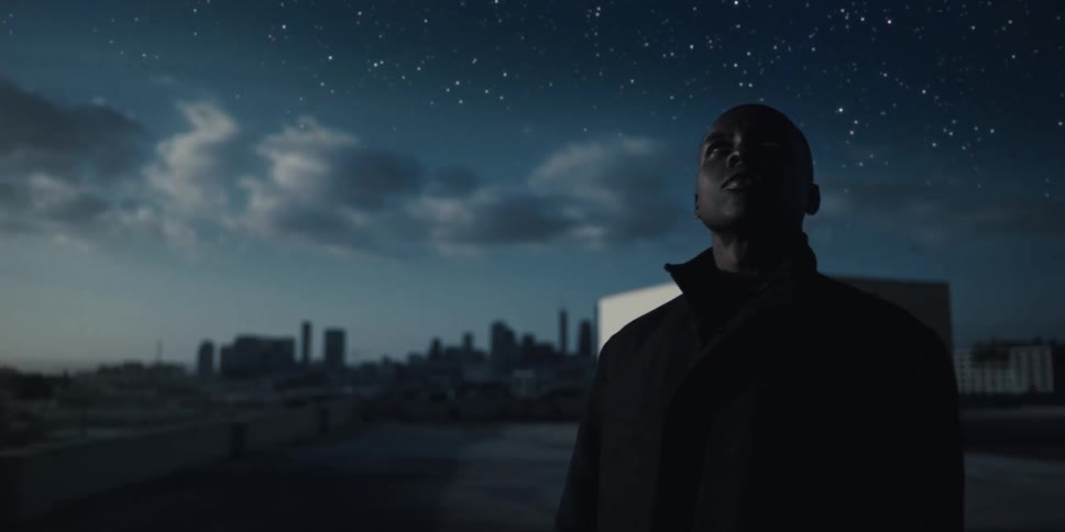 Man standing on the roof of a building next to the city looking at the starry night sky