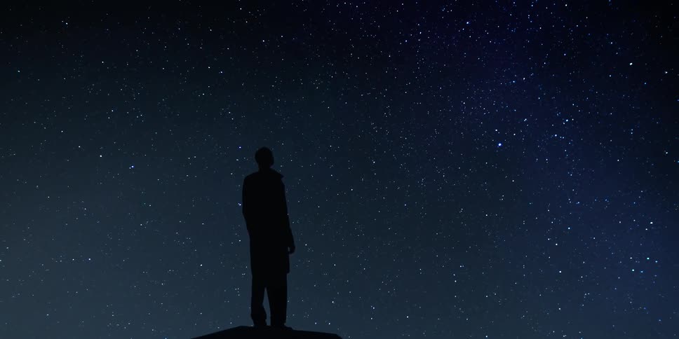 Silhouette of a person standing outside on a dark starry night looking at the sky