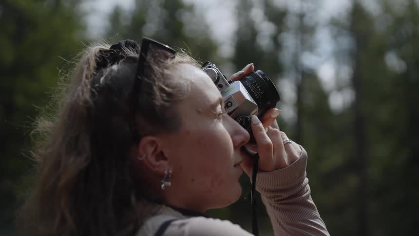 Woman holds camera to her eye standing in forest