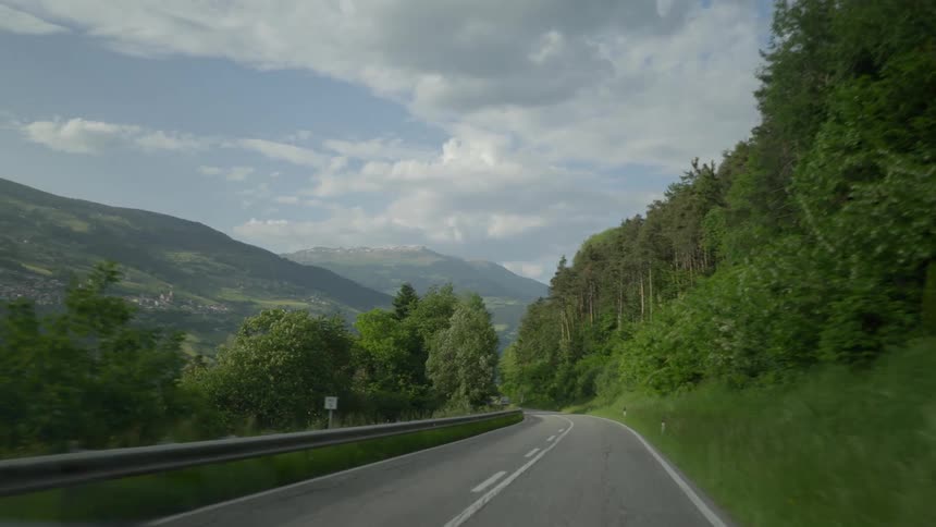 Traveling downhill on a forested mountain road under a cloudy sky