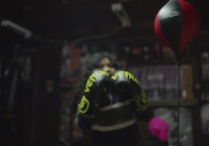 A young girl wearing boxing gloves as she punches a bag hung from the ceiling