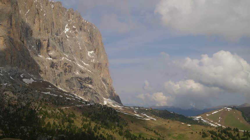 Large mountain cliffs with snow in the ridges and pine trees at the base on the hill