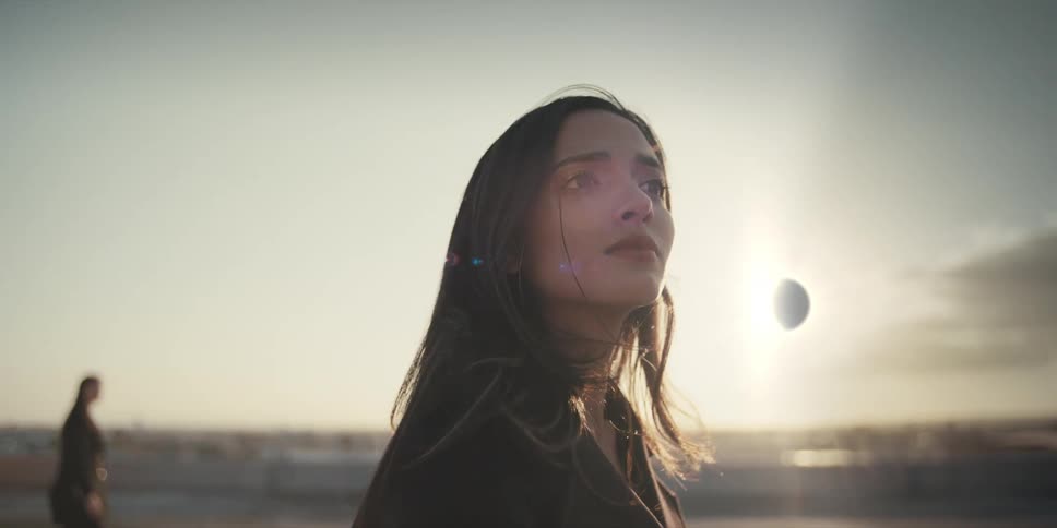 Close up of a woman looking up and out away from her as the sunlight shines against her back and silhouettes of people walk by