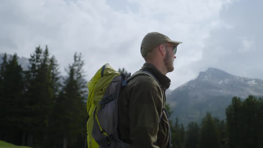 A man in a hat and glasses with a camping backpack looking to the sides