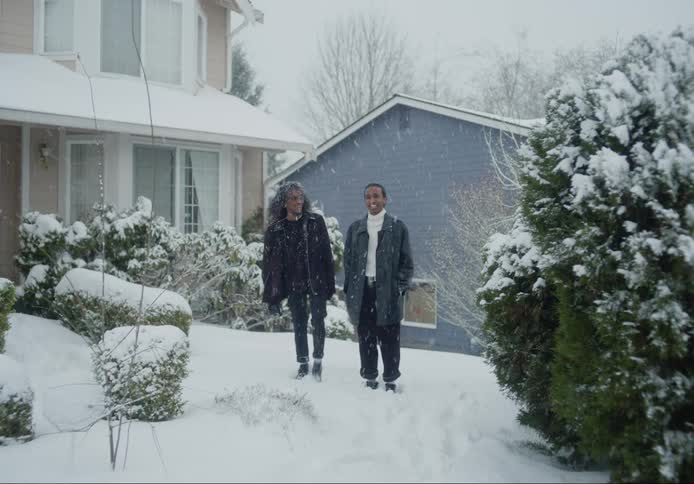 A man and woman stand outside a house while its snowing outside