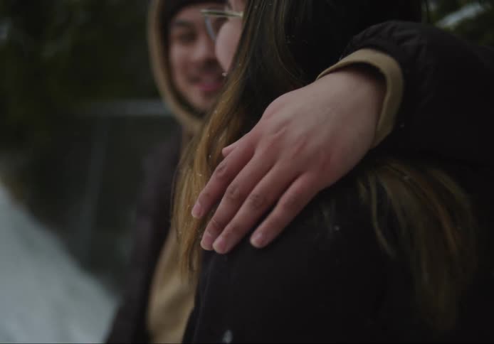 Man with his arm around a womans shoulder engaged in a smiling conversation in an outdoor space with snow
