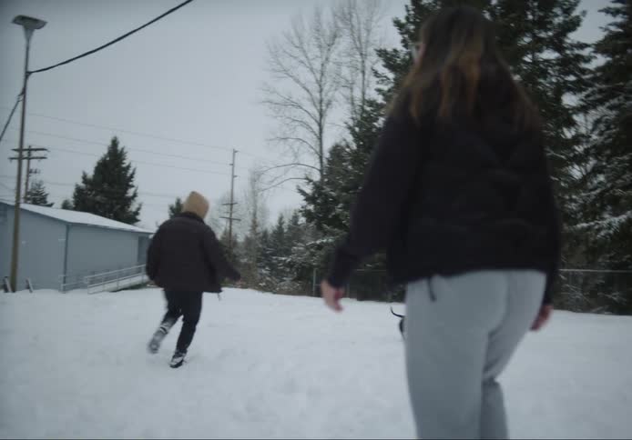 A man and a woman are outside playing with their small dog running in the snow