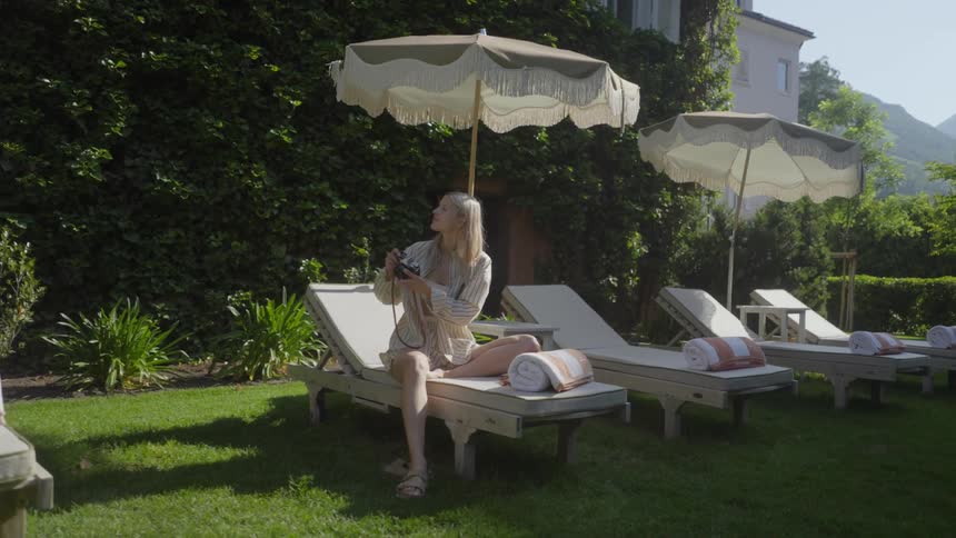 Young blonde woman sitting in an outdoor setting taking photos with her camera