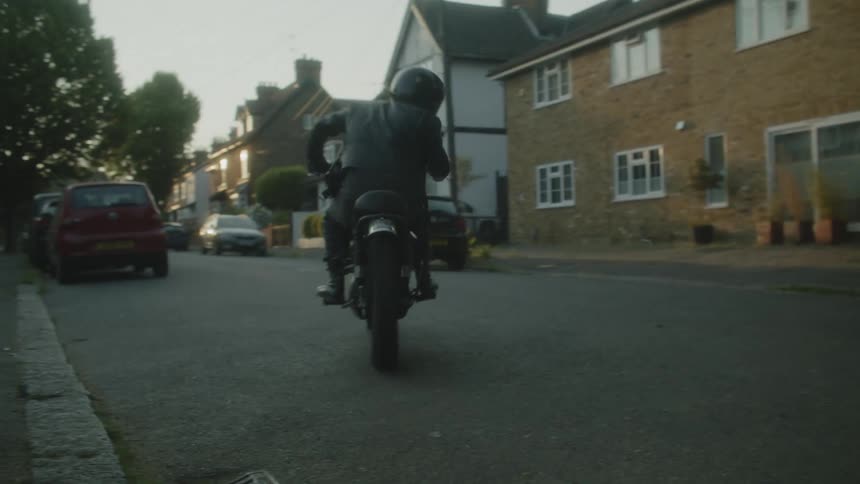 A person wearing a helmet driving away on a motorcycle on a street near houses in the day time
