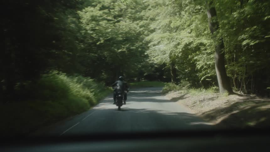 A biker riding his motorcycle on a road surrounded by trees
