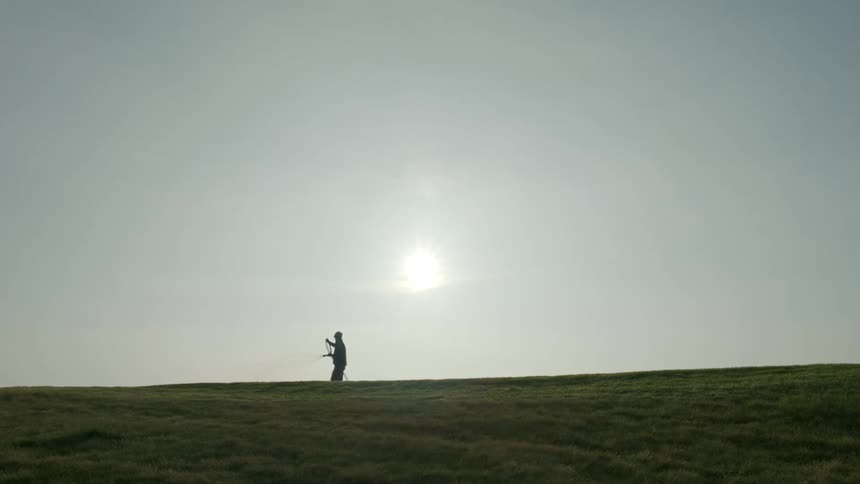 Person walks across grassy field with watering hose