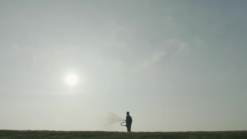 Man watering golf course is silhouetted against the sun