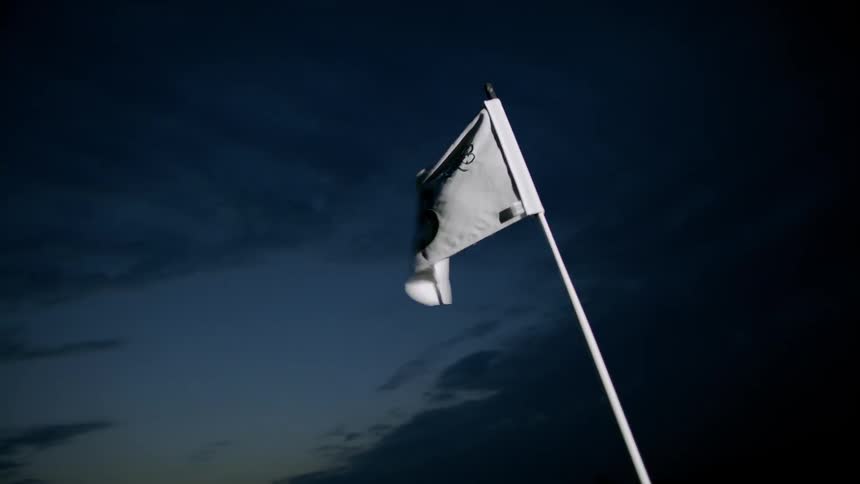 Light shines on a white flag with the number 18 as it waves under a darkening sky