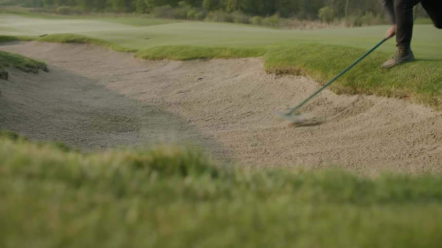 Man rakes the sand trap bunker in golf course