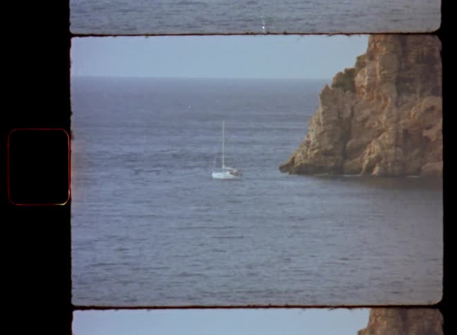 White sail boat or sailing yacht floating in front of giant rocky cliff or high coast in the ocean leaving protected bay entering open sea with high waves setting sail and starting into new adventure with challenging experiences on vintage Super-8 film