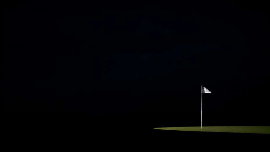 A golf course flagpole with the banner blowing in the wind surrounded by darkness