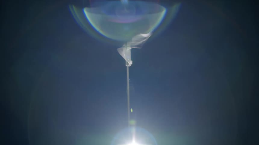 Rings of light reflect as a white flag rapidly waves under a darkening sky