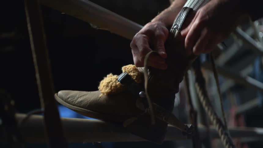 Cowboy strapping on his boots at a rodeo